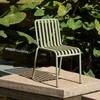 HAY Palissade Gartenstuhl aus Metall in Olivgrün, modernes Design, auf Betonplattform neben Wasser mit Laub. - Special Edition Palissade Gartenstuhl