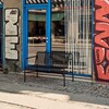 HAY Palissade Outdoor-Bank in Anthrazit, robustes Metall-Design, vor urbanem, blauem Ladenfenster und Kopfsteinpflaster. - Palissade Dining Gartenbank