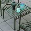 HAY Palissade Outdoor-Möbelkollektion mit grünem Metalltisch und Stühlen, Kanne und Tasse auf Terrasse. - Palissade Ottoman/ Gartenbeistelltisch 2er Set