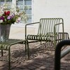 HAY Palissade Gartenstuhl und -bank aus Metall in Olivgrün auf Kopfsteinpflaster mit Blumenschmuck im Vordergrund - Palissade Garten Loungesessel niedrig 2er Set