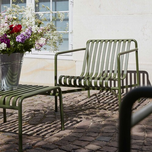 HAY Palissade Gartenstuhl und -bank aus Metall in Olivgrün auf Kopfsteinpflaster mit Blumenschmuck im Vordergrund - Palissade Garten Loungesessel niedrig 2er Set